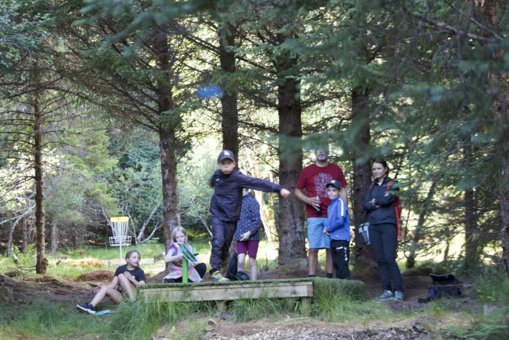 Magnus Thuv Nilsen (12) midt i et kast på Borg frisbeegolfbane lørdag. Bak til høyre står bror Henrik, far Fredrik og mor Sylvi og ser på. Foto: Eirik Husøy