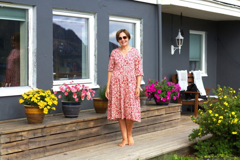 Lærer, sanger og nyutnevnt korleder Agnes Gjertsen, kledd i blomsterkjole blant blomster. I et intervju med Avisa Lofoten forteller hun om planene for Demenskoret og veien som ledet henne til å ta på seg utfordringen som korleder. Foto: Eirik Husøy